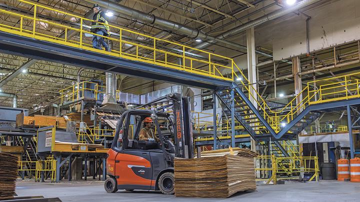 A forklift operating inside West Fraser’s Williams Lake Plywood facility while a worker walks along an overhead catwalk, illustrating pedestrian safety around mobile equipment on work sites.