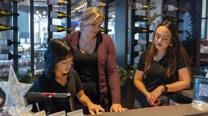 Restaurant staff stand together near a point-of-sale counter in a hospitality setting.