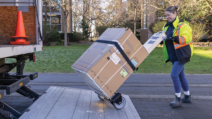 A woman smiling while loading boxes using a dolly into a loading truck