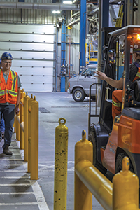A forklift operating in an industrial facility as a worker in high-visibility gear walks nearby along a designated pedestrian pathway, illustrating measures to prevent of struck-by incidents around mobile equipment.