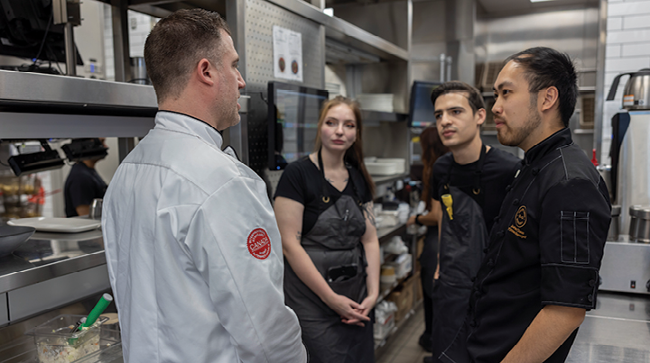 Restaurant staff gathered in a commercial kitchen for a workplace discussion.