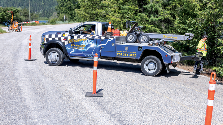 Tow truck parked on the roadside beside traffic cones while a worker prepares equipment near the shoulder.