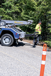 Tow truck parked on the roadside beside traffic cones while a worker prepares equipment near the shoulder.