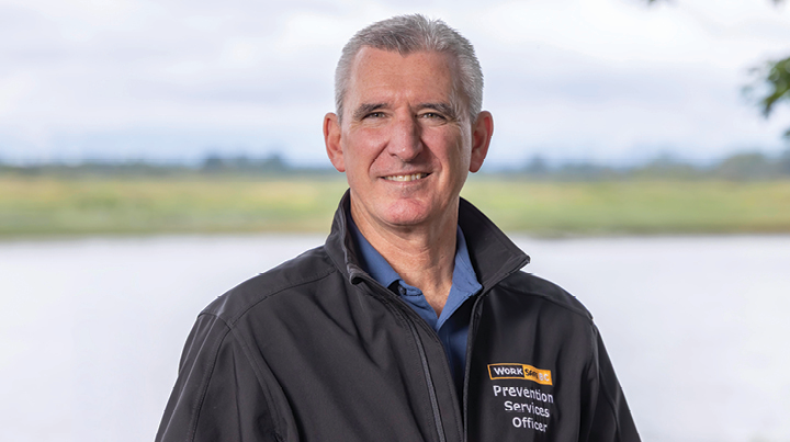 Prevention services officer wearing a WorkSafeBC jacket standing outdoors near a body of water.