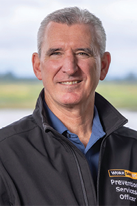 Prevention services officer wearing a WorkSafeBC jacket standing outdoors near a body of water.