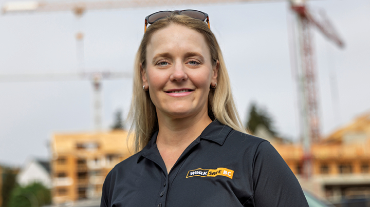 Person wearing a black WorkSafeBC-branded shirt standing outdoors at a construction site, with cranes and partially built structures visible in the background.